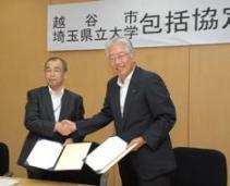協定書にサイン後、握手をする板川市長と佐藤学長