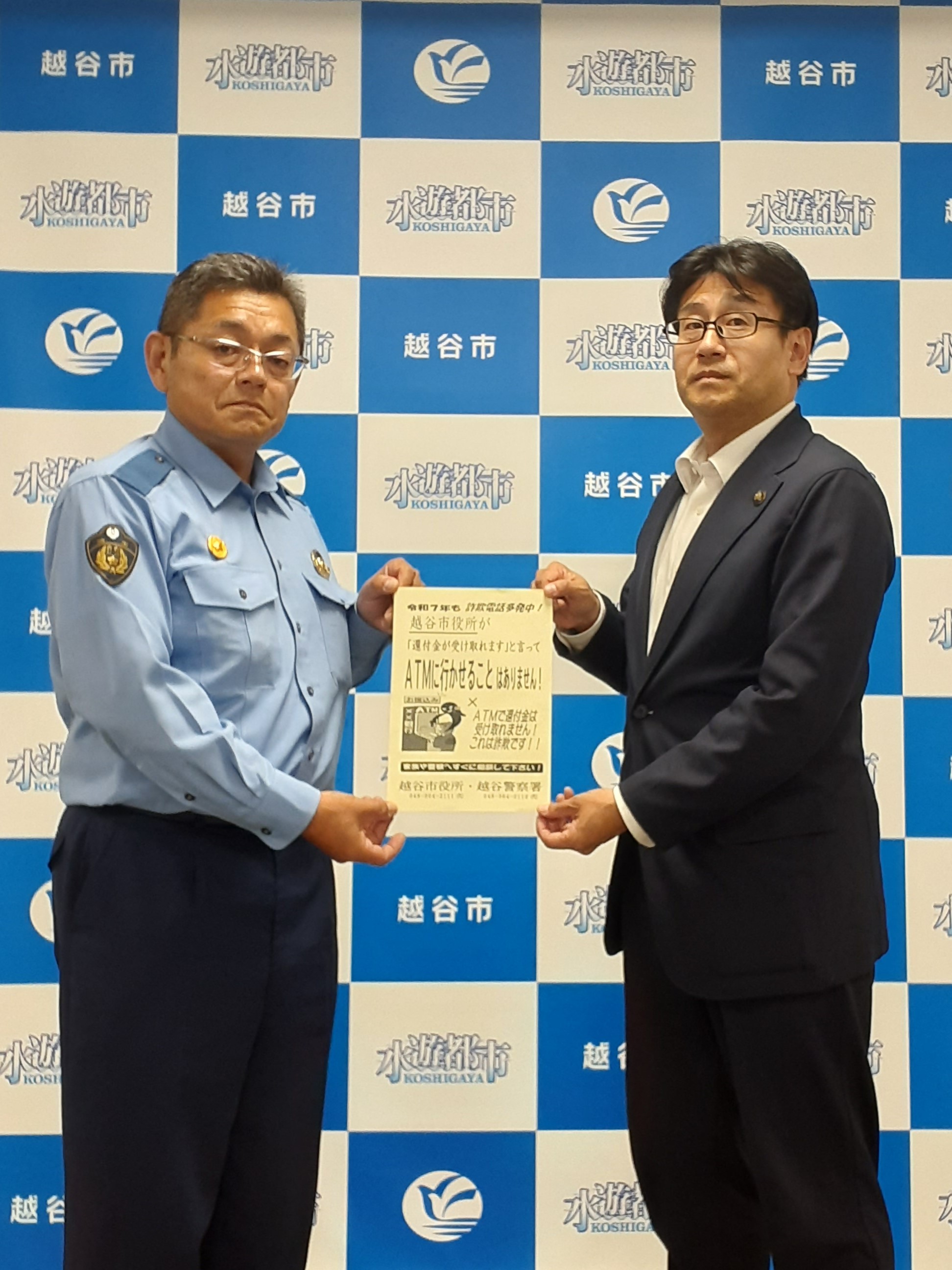 チラシを渡す越谷警察署長と受け取る越谷市長の画像